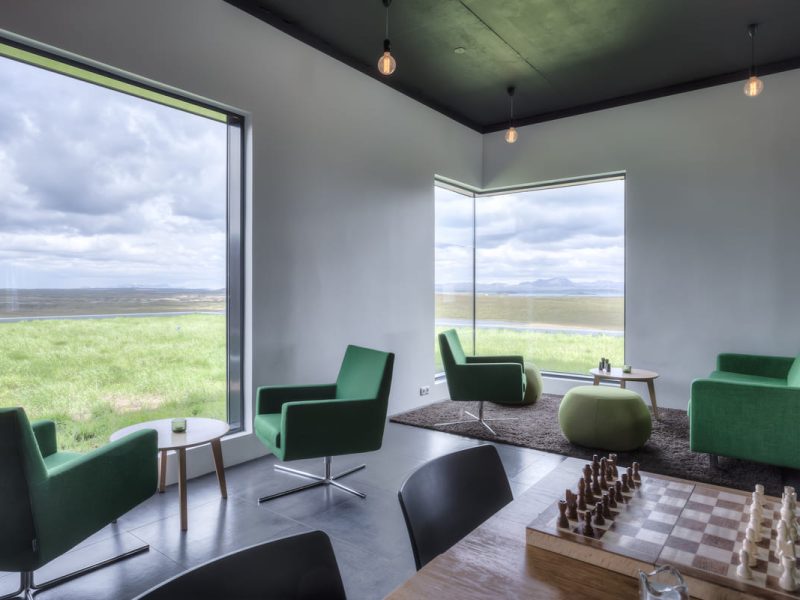 Cozy lounge area with green chairs, chess set, and panoramic view of Lake Myvatn at Hotel Laxa.